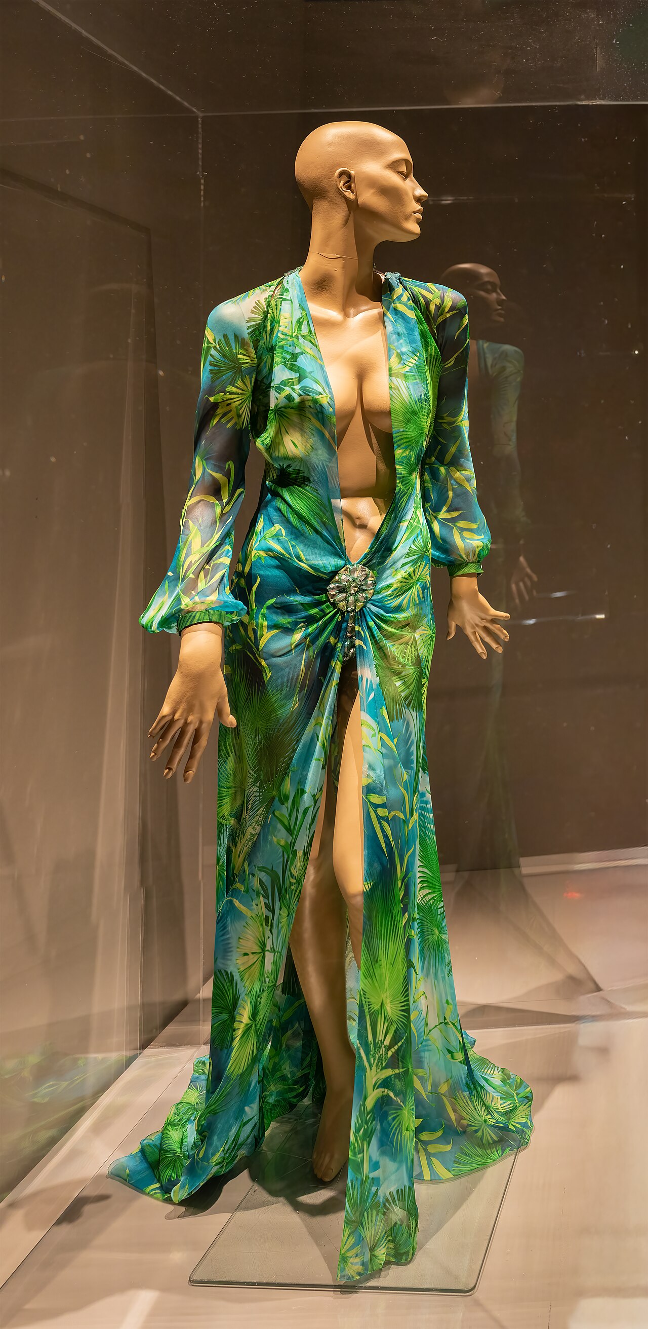 The original green jungle-print silk chiffon Versace dress from 2000, displayed on a mannequin in a glass case at The Museum at FIT, New York